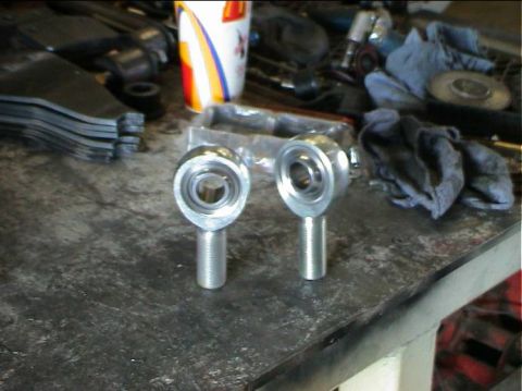 1979 Ford Bronco - Two rod end bearings are shown on a cluttered workbench, likely for an automotive upgrade.