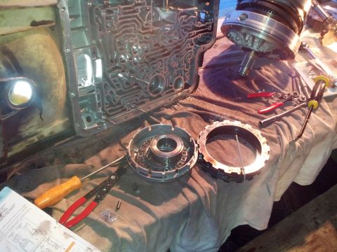 1995 Ford Bronco - Disassembled transmission valve body and clutch pack components laid out on a workbench with tools.