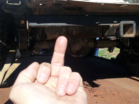 1986 Ford Bronco - A hand is shown giving the middle finger in front of the undercarriage of a vehicle, focusing on the rear axle and hitch.