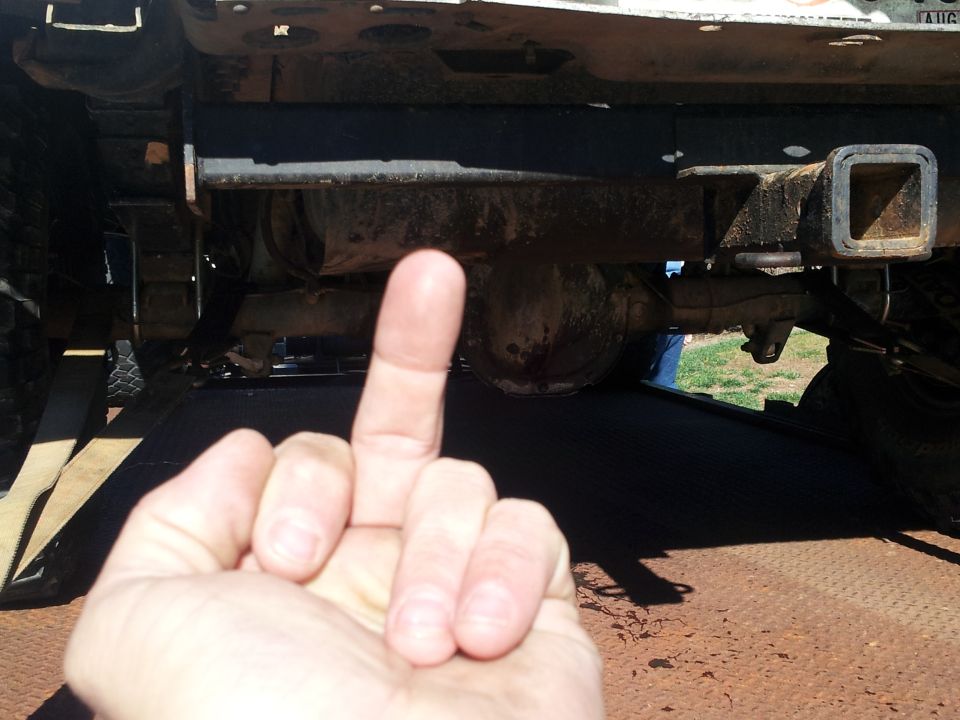 hand giving middle finger in front of vehicle's rear axle and hitch