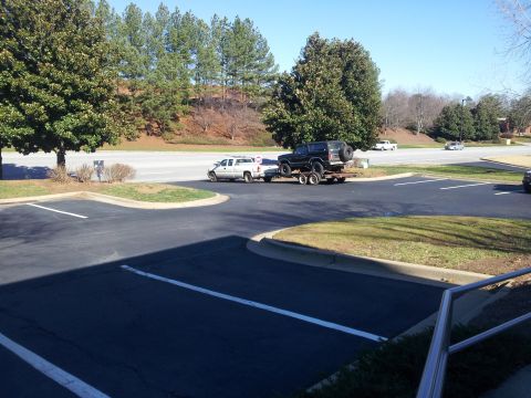 1986 Ford Bronco - A black SUV is transported on a trailer pulled by a white pickup truck on a sunny day.