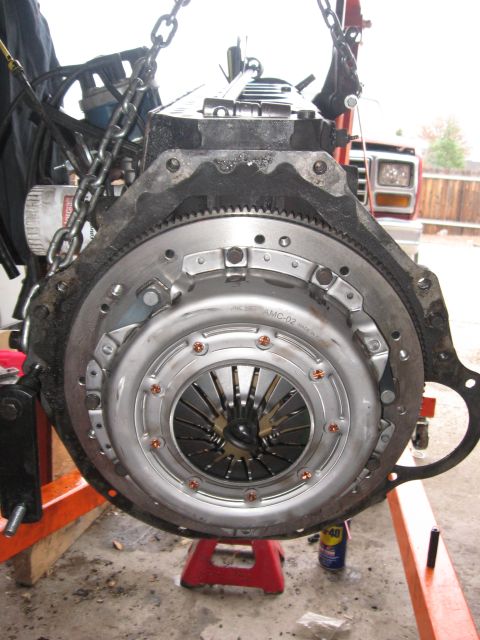 1981 Ford Bronco - Engine clutch assembly being worked on, with a portion of a red truck visible in the background.