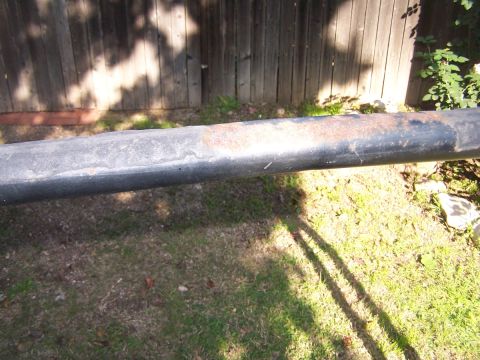 1990 Ford Bronco - A close-up view of a black roll bar showing areas of rust and wear against a wooden fence background.
