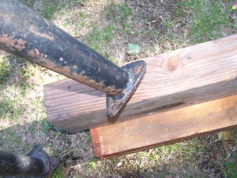 1990 Ford Bronco - Close-up of a black roll bar mount secured to wooden planks on a grassy surface.