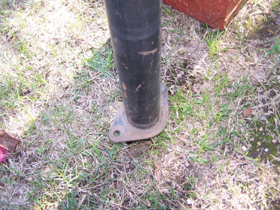 Metal pole with a rusted flange bolted to the ground