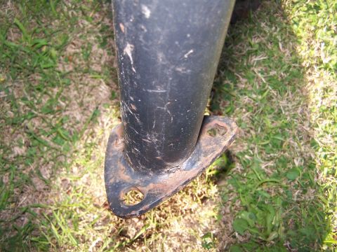 1990 Ford Bronco - Close-up of a black metal pipe with a rusty mounting bracket, resting on grass.