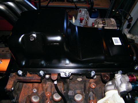 2004 Ford Crown Victoria - Close-up of an engine oil pan attached to a block, with exhaust headers in the background.