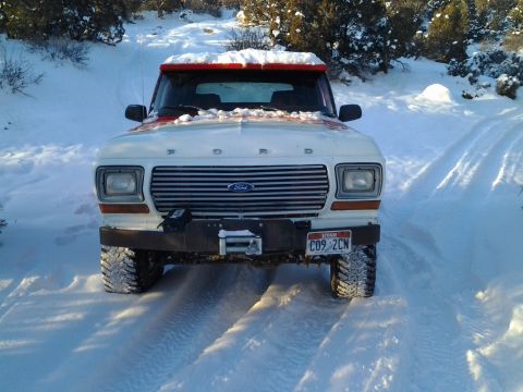 1979 Ford Bronco - A white Ford Bronco with red trim navigates a snowy path, equipped with an aftermarket bumper and winch.