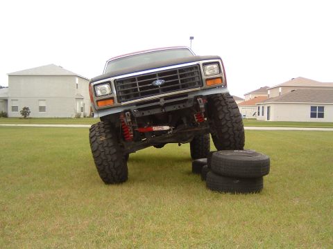 1983 Ford Bronco - A lifted Ford Bronco is positioned on a grassy lawn with stacked tires beneath its front wheels.