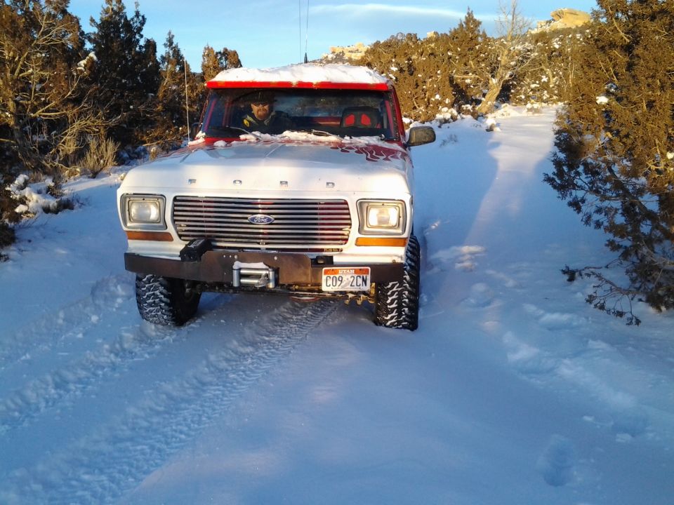 1979 Ford Bronco driving on a snowy road with trees on either side
