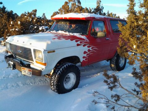 1979 Ford Bronco - A lifted Ford Bronco with flame decals sits in a snowy landscape under a clear blue sky.