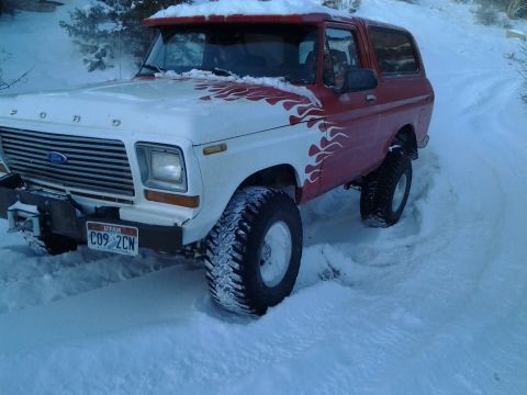 1979 Ford Bronco - This red and white 1979 Ford Bronco navigates a snowy path, its flame decals visible.