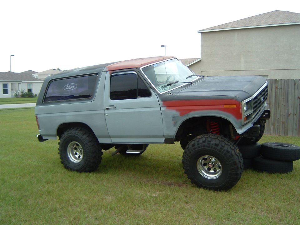 Lifted 1980s Ford Bronco in primer gray with red fender flares and roof