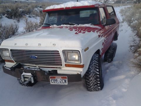 1979 Ford Bronco - This lifted Ford Bronco navigates a snow-covered path, its flame decals visible against the white and red paint.