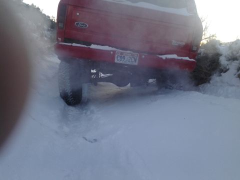 1979 Ford Bronco - This red 1979 Ford Bronco is seen from the rear as it drives through a snowy terrain, kicking up snow.