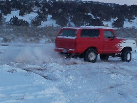 1979 Ford Bronco - This SUV is kicking up snow as it drives through a snowy landscape.