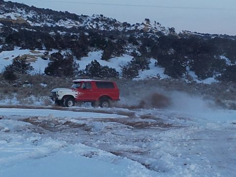 1979 Ford Bronco - A red and white 1978 Ford Bronco navigates a snowy terrain, creating a cloud of dust.