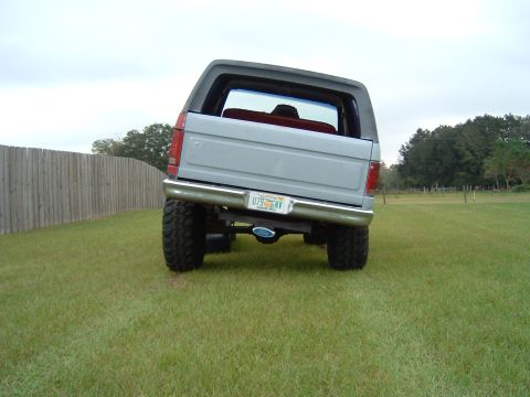 1983 Ford Bronco - Rear view of a lifted 1983 Ford Bronco parked on grass with a wooden fence in the background.