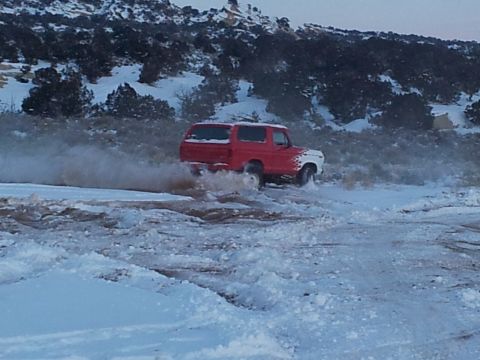 1979 Ford Bronco - A red and white 1979 Ford Bronco kicks up snow and mud while driving off-road.