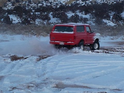 1979 Ford Bronco - A red 1979 Ford Bronco navigates a snowy, off-road path, spraying snow from its tires.