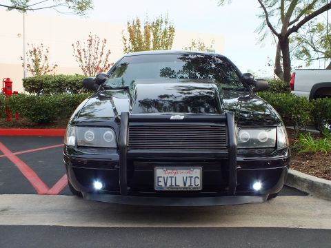 2003 Ford Crown Victoria - Blacked-out Crown Victoria sedan showing halo projector headlights, brush guard and lit driving lamps.