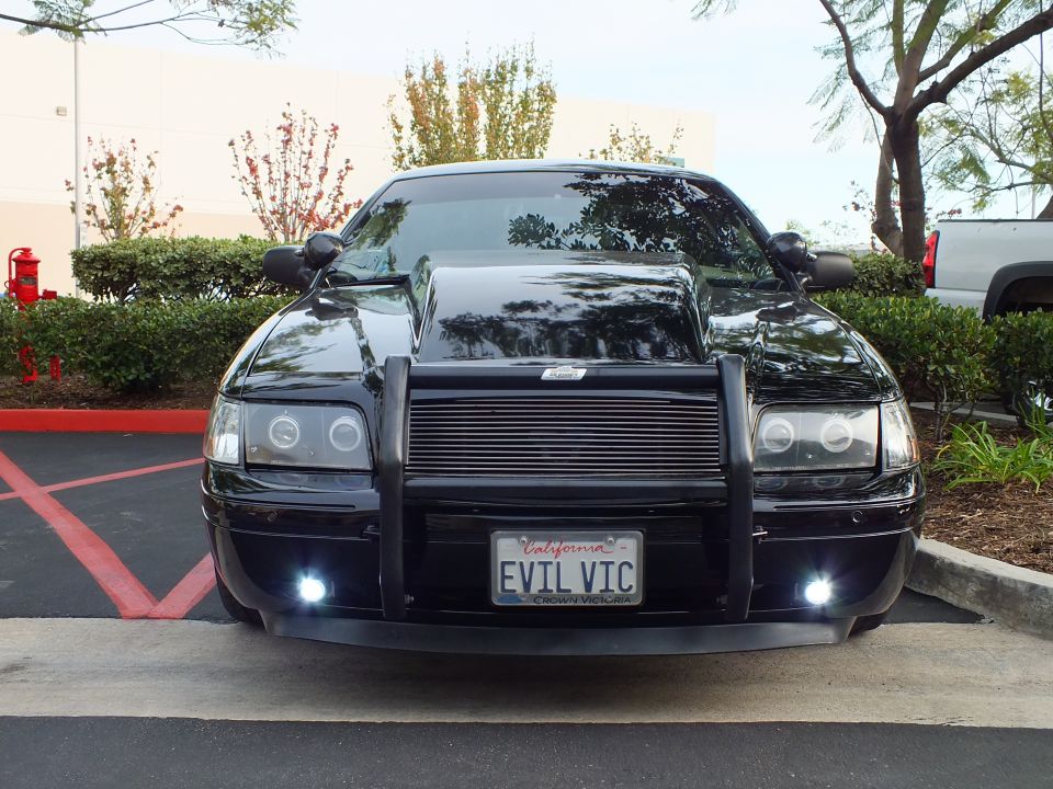 Black Crown Victoria with billet grille and EVIL VIC plate parked at angle in red-curb lot