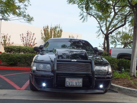 2003 Ford Crown Victoria - Front of a blacked-out Crown Victoria sedan with halo headlights and EVIL VIC plate in a parking lot.
