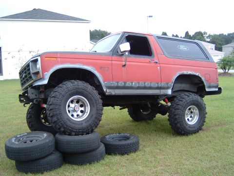 1983 Ford Bronco - This modified Ford Bronco sits high on large off-road tires, with spare tires piled nearby.