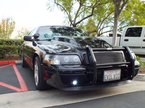 2003 Ford Crown Victoria - Angled front view of a blacked-out Crown Victoria sedan with push bar and amber turn-signal headlights.