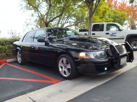 2003 Ford Crown Victoria - Side three-quarter view of a blacked-out Crown Victoria parked beside a white Baker Hughes pickup.