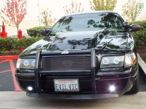 2003 Ford Crown Victoria - Glossy black sedan with EVIL VIC plate and Crown Victoria frame, lit fog lights and chrome push bumper.