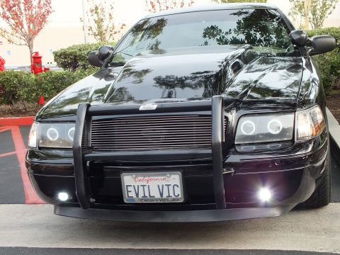2003 Ford Crown Victoria - Black Ford sedan front, EVIL VIC plate and Crown Victoria frame, lit fog lights below billet grille.