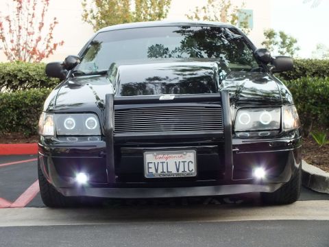 2003 Ford Crown Victoria - Black sedan front, dual halo headlights and billet grille, EVIL VIC California plate at a lot.