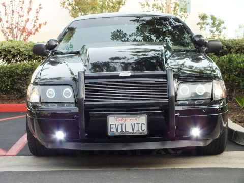 2003 Ford Crown Victoria - Glossy black Ford sedan front, lit fog lamps and EVIL VIC tag with Crown Victoria frame.