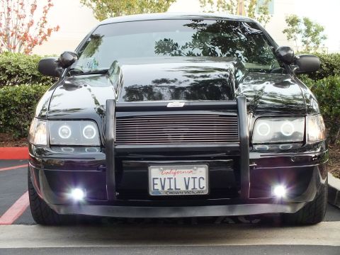 2003 Ford Crown Victoria - Black sedan front fascia, push bar and chrome wheels, EVIL VIC plate over lit fog lights.