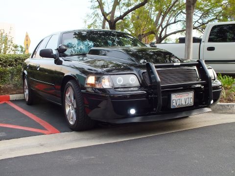 2003 Ford Crown Victoria - Angled front of a glossy black sedan with chrome wheels and grille guard, EVIL VIC California tag.