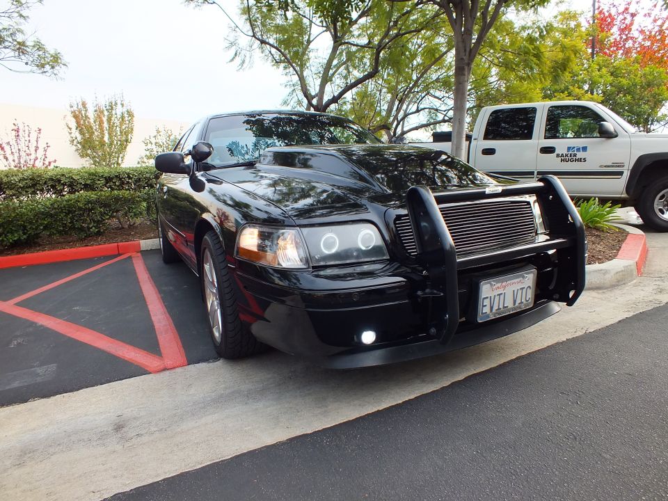 Black Crown Victoria front three-quarter showing halo lights, grille guard and EVIL VIC plate