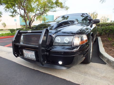 2003 Ford Crown Victoria - Close low angle of a black Ford sedan front, billet grille and lit fog lamp, EVIL VIC California tag.