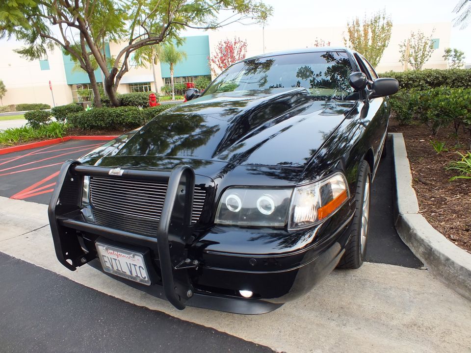 Black Crown Victoria front three-quarter showing halo headlights, grille guard and chrome wheels