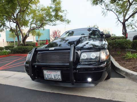 2003 Ford Crown Victoria - Front three-quarter of a blacked-out Crown Victoria sedan, push bar and projector halo headlights, lot setting.
