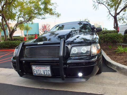 2003 Ford Crown Victoria - Police-style Crown Victoria parked in lot, grille guard and billet insert visible, projector halo lamps lit.