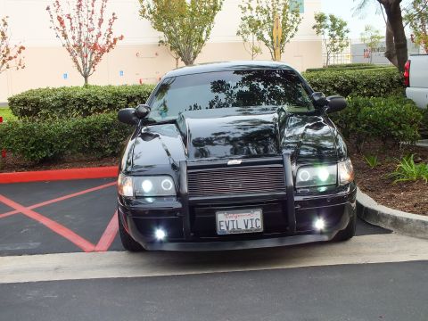 2003 Ford Crown Victoria - Wider front view of a black Crown Victoria in a parking stall, grille guard and lit foglights visible.