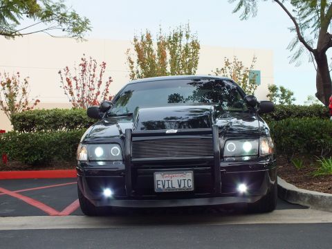 2003 Ford Crown Victoria - Front view of a black Crown Victoria in a lot, grille guard and billet grille, halo lamps and foglights lit.