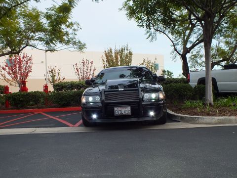 2003 Ford Crown Victoria - Wider front view of a black Crown Victoria in a parking stall, grille guard and foglights, SUV at right.