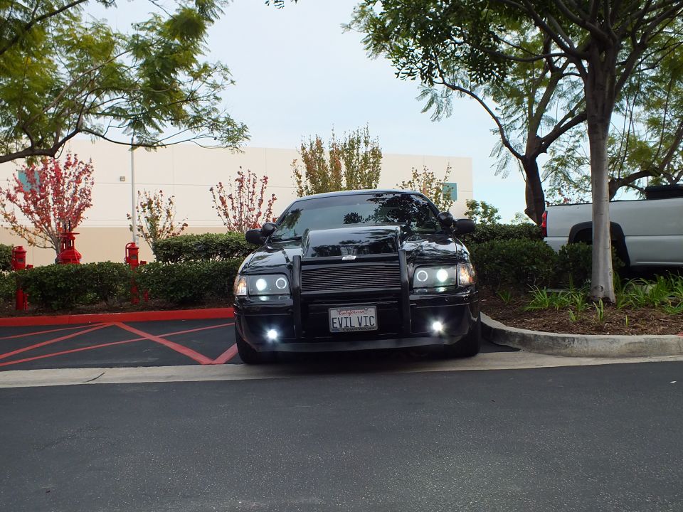 Black Ford Crown Victoria parked in lot, push bar, halo lamps, EVTL VTC plate, SUV behind