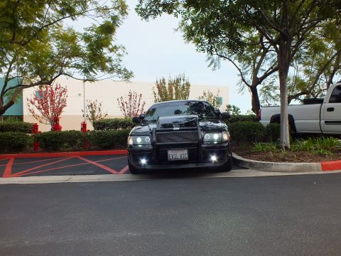 2003 Ford Crown Victoria - Lowered black Crown Victoria sedan, custom grille guard and projector halos, viewed across parking lot.