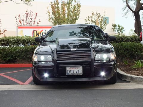2003 Ford Crown Victoria - Front-on shot of lowered black sedan with billet grille and push bar, Domino's sign behind.