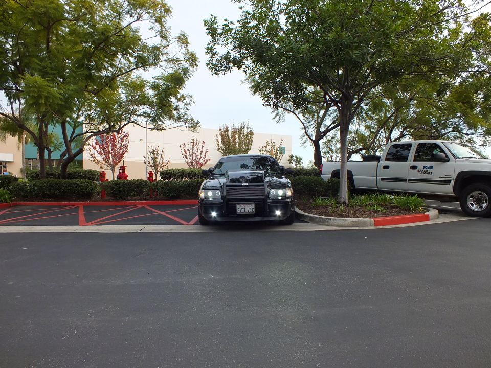 Distant front view of black Crown Victoria with push bar parked beside white pickup