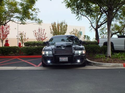 2003 Ford Crown Victoria - Front view of lowered black Crown Victoria with push bar parked near shrubs and white truck.