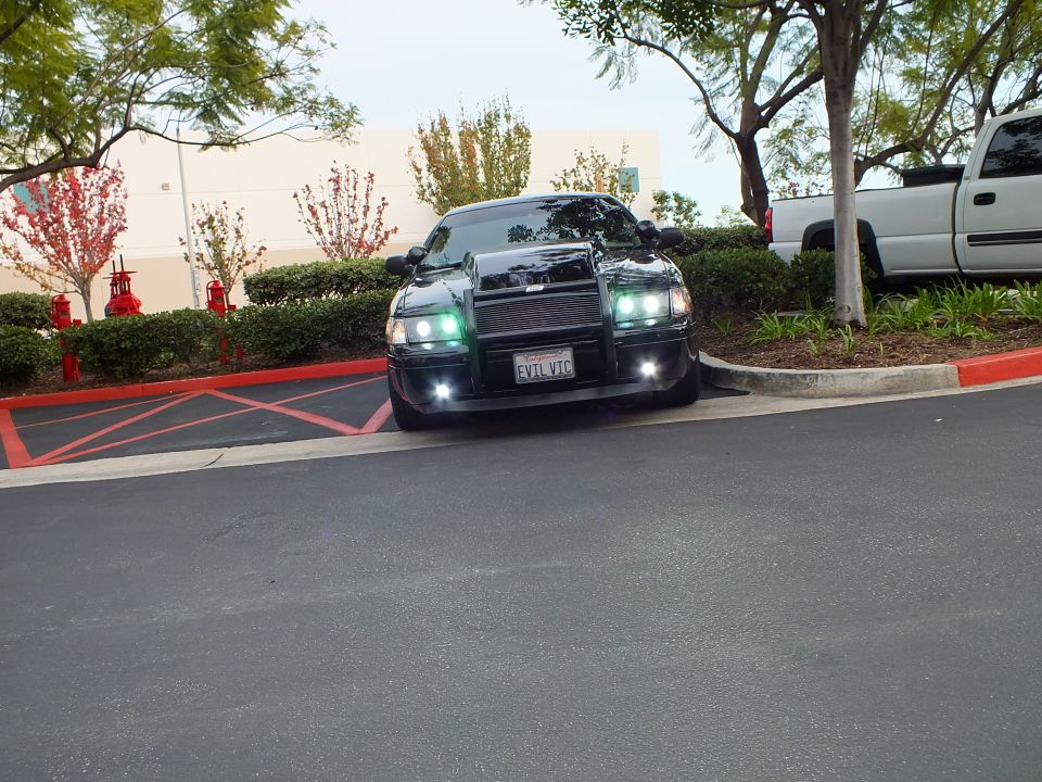 Black sedan with push bar and halo headlights parked at curb, EVIL VIC plate